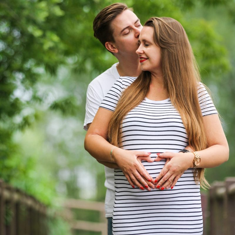 Familienbild von Mann küsst seine schwangere Frau mit Händen am Babybauch in Oberkrämer am Mühlensee
