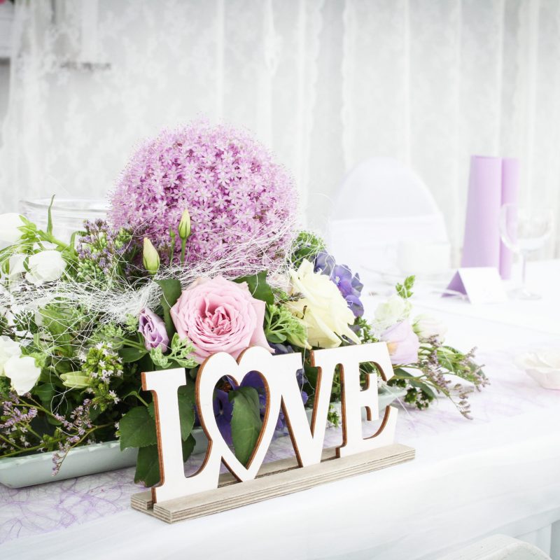 Love Schriftzug aus Holz vor lilafarbenen Blumen und Hochzeitsdekoration