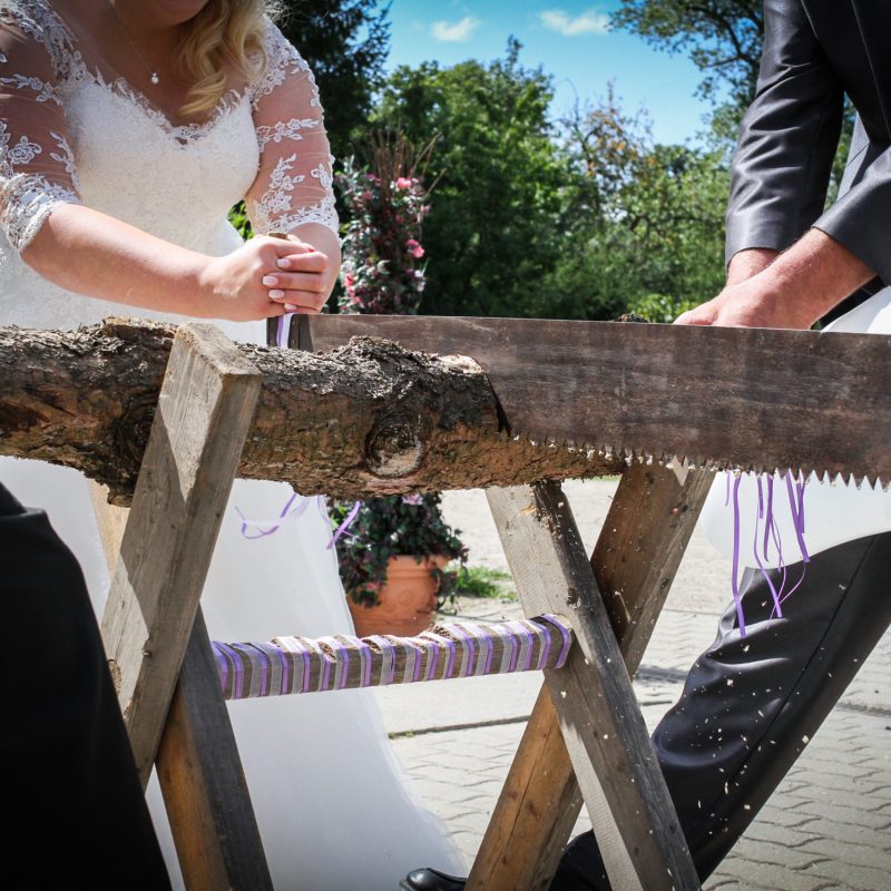 Hochzeitsbild von Brautpaar beim traditionellen gemeinschaftlichem Baumstammsägen in Kremmen