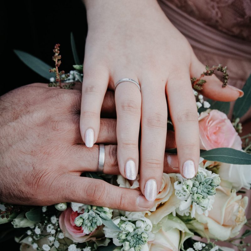 Hochzeitsbild von Händen mit Eheringen mit Brautstrauss