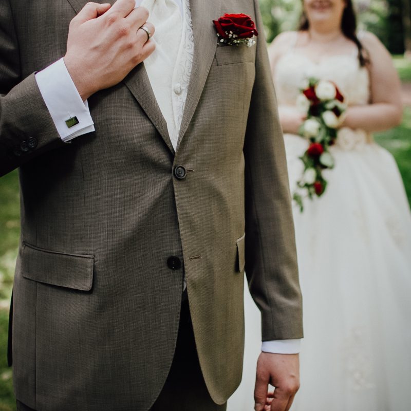 Hochzeitsbild von Bräutigam mit personalisiertem Manschettenknopf und Braut im Hintergrund